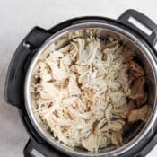 An Instant Pot with cooked, shredded chicken inside.