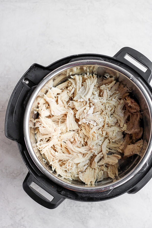 An Instant Pot with cooked, shredded chicken inside.