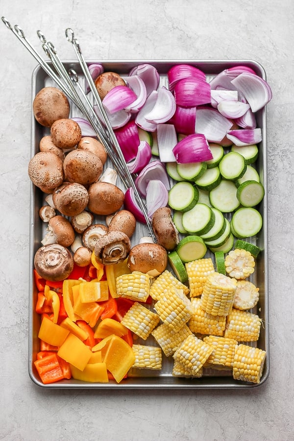 Fresh veggies and metal skewers on a baking sheet.