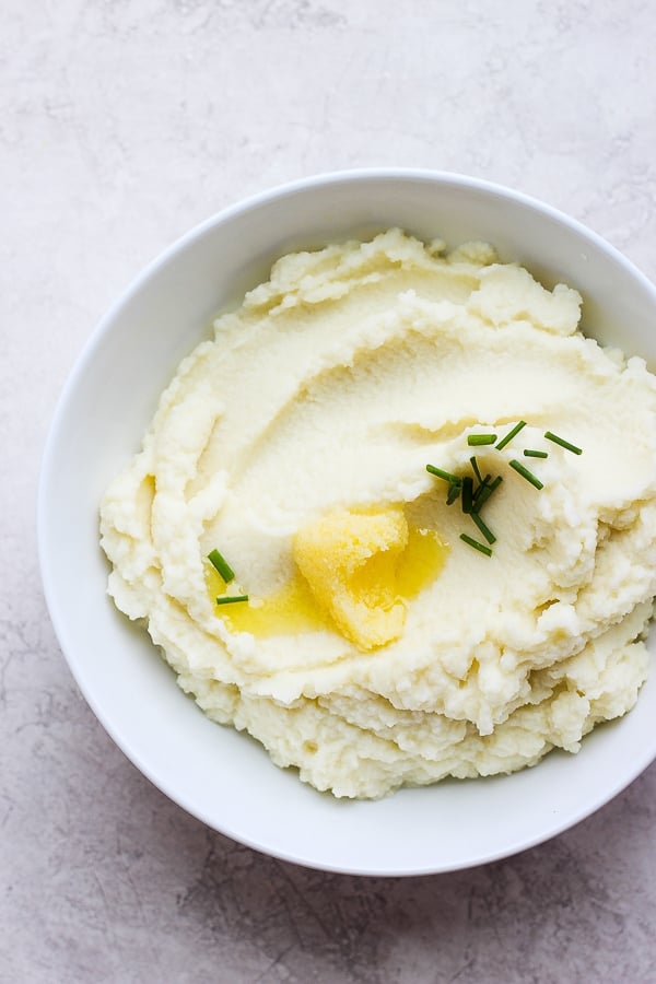 Cauliflower mash in a white bowl with melted ghee on top.