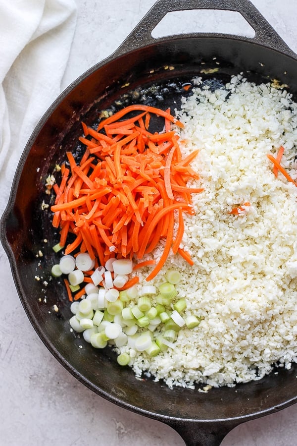 Cauliflower rice, onion and carrots in a cast iron skillet. 