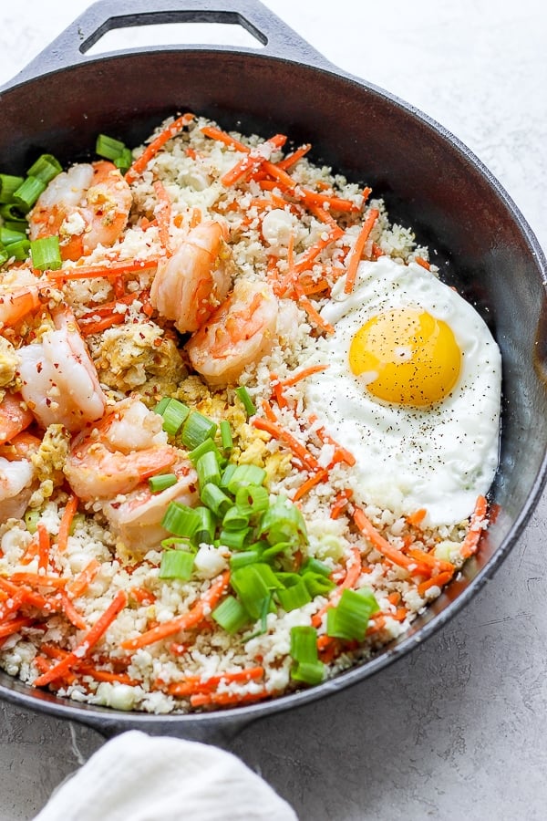 shrimp fried cauliflower rice in a cast iron skillet with fried egg on top. 