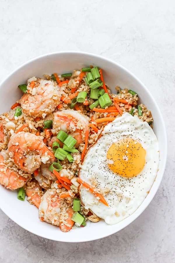 Shrimp fried cauliflower rice in a bowl with a fried egg on top. 