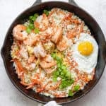 A cast iron skillet filled with shrimp fried cauliflower rice with a fried egg on top.