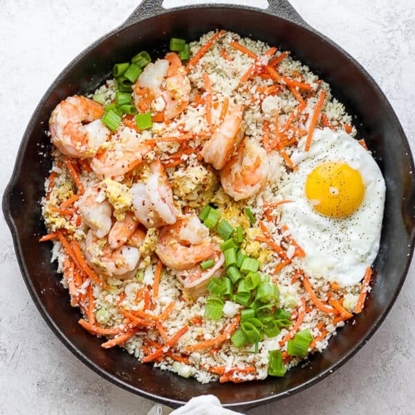 A cast iron skillet filled with shrimp fried cauliflower rice with a fried egg on top.