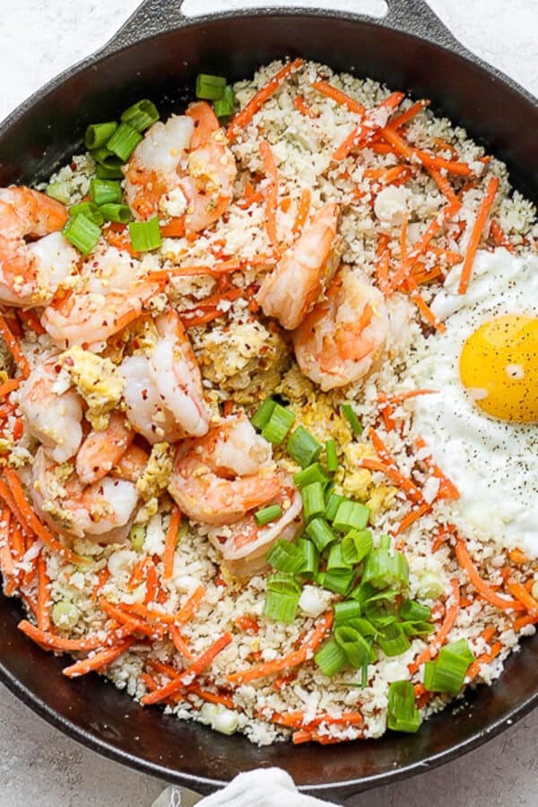 A cast iron skillet filled with shrimp fried cauliflower rice with a fried egg on top.