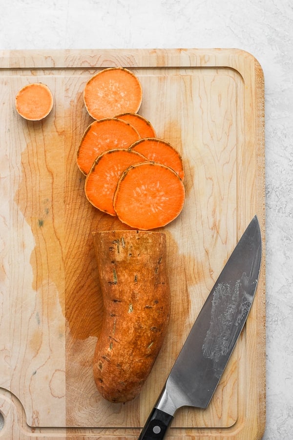 Cutting board with a half sliced sweet potato and chef knife. 