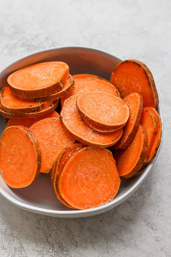 Bowl of sliced sweet potatoes covered in olive oil and sprinkled with salt and pepper. 