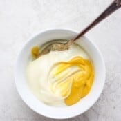 Mustard and mayonnaise in a white bowl with a spoon before mixing.