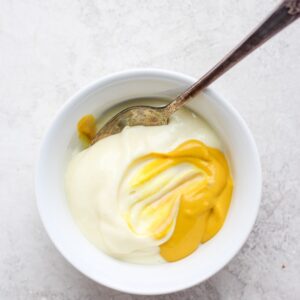 Mustard and mayonnaise in a white bowl with a spoon before mixing.