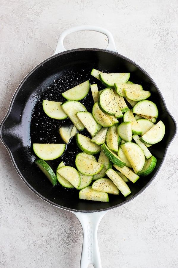 Zucchini slices added to the pan with melted ghee, salt, and pepper.