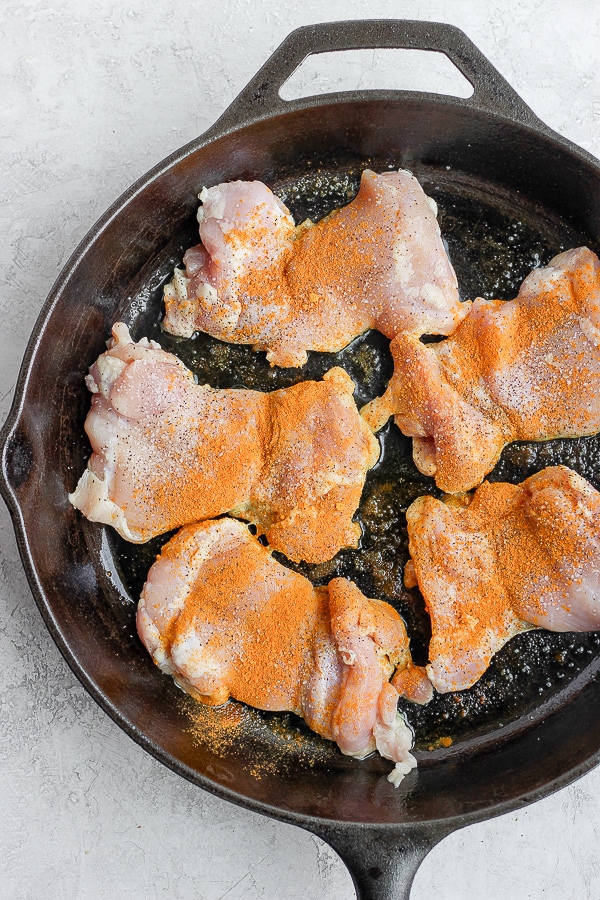 Boneless chicken thighs in a cast iron skillet sprinkled with salt, pepper and turmeric. 