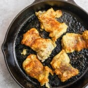 Boneless, skinless chicken thighs searing in a large cast iron skillet.
