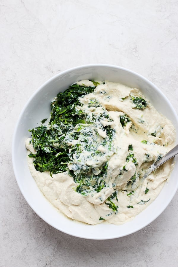 Spinach mixed into the ricotta mixture in a white bowl.