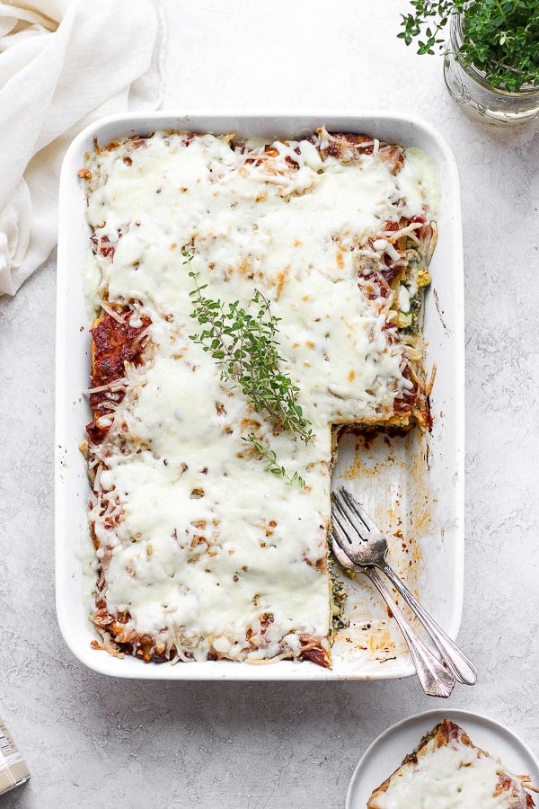 A fully baked dairy-free lasagna in a white baking dish and a large piece was removed.