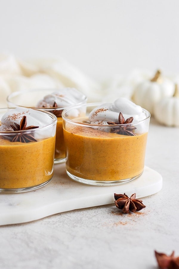 Three small glasses of pumpkin pudding with whipped topping.