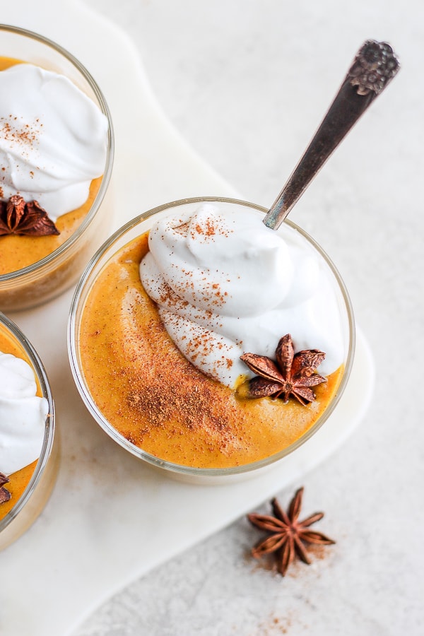 Pumpkin pudding in a small glass with some whipped coconut cream on top.