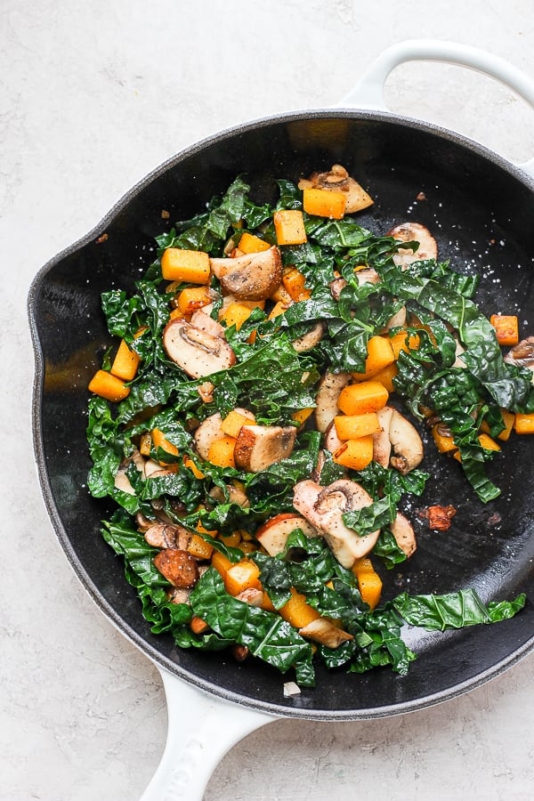 Shallots, garlic, squash, mushrooms, and kale sautéing in a cast iron skillet.