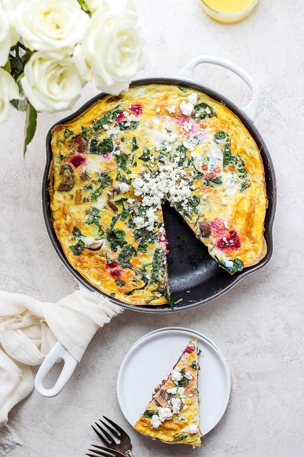 A fully cooked vegetable frittata with one slice removed and on a plate.