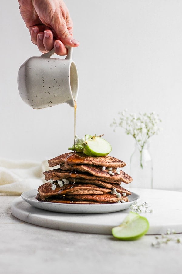 Syrup being poured on a stack of apple pancakes.