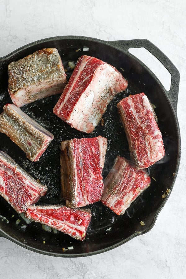 Short ribs searing in a cast iron skillet. 