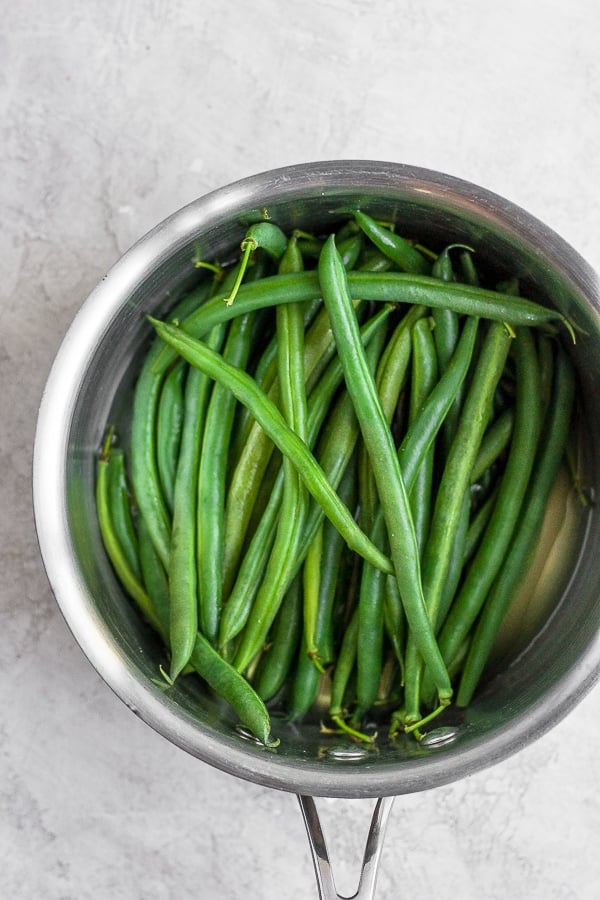 Fresh green beans in a saucepan with a shallow amount of water in the bottom.