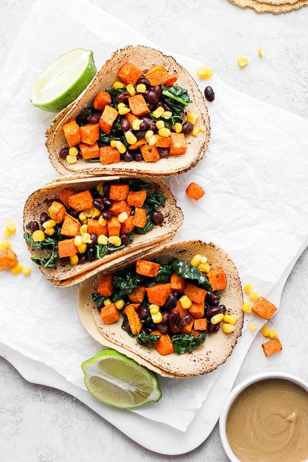 Three assembled sweet potato tacos on a piece of parchment paper.