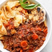Bowl of short rib ragu with noodles, basil and garlic.