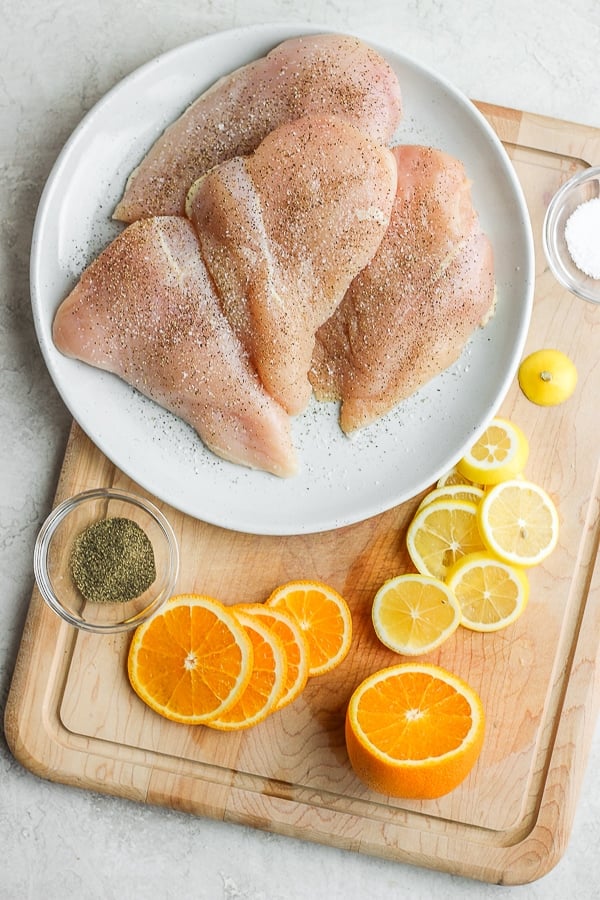 Seasoned chicken breasts on a white plate next to slices of oranges and lemon.