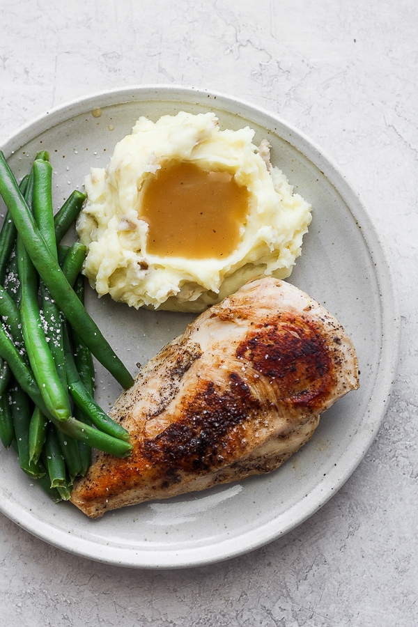 Sous vide chicken breast on a plate with mashed potatoes and green beans.