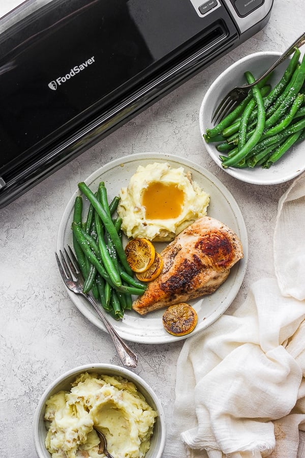 Sous vide chicken with sides on a plate next to a FoodSaver Preservation System.