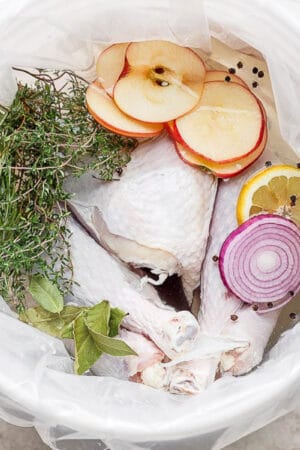 A turkey sitting in a brine solution with herbs, apples, lemon and red onion.
