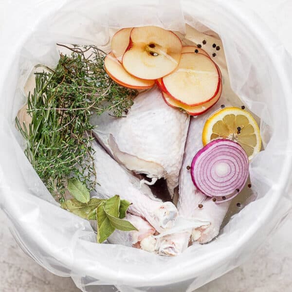 A turkey sitting in a brine solution with herbs, apples, lemon and red onion.