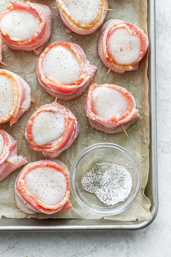 Scallops wrapped in bacon and secured with toothpicks on parchment-lined baking sheet.