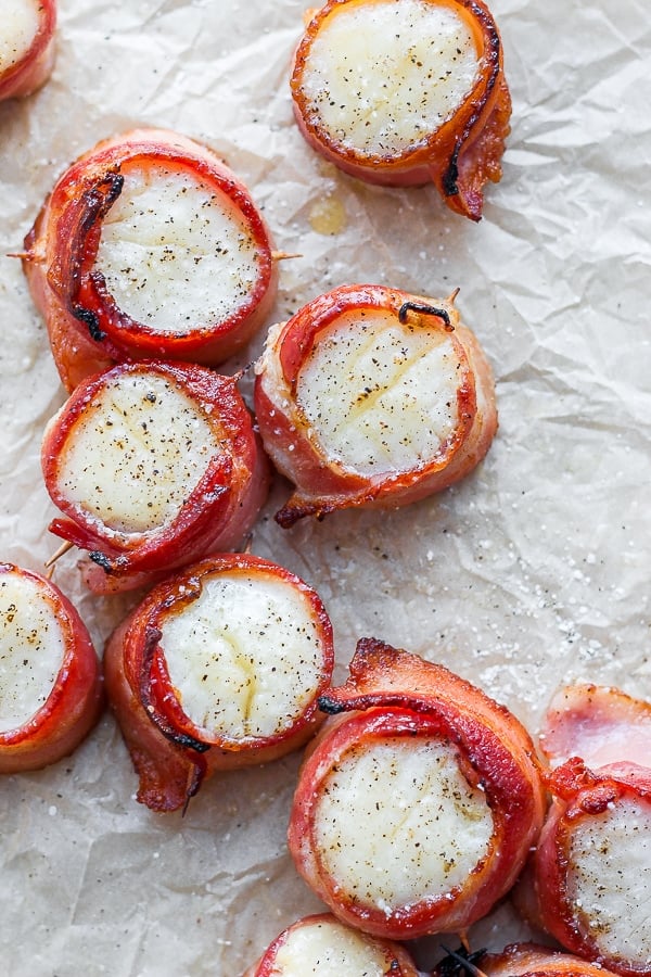 Cooked bacon wrapped scallops on parchment paper.