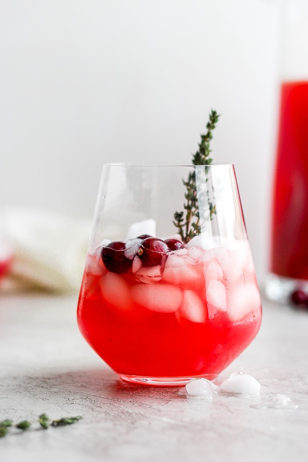Glass of holiday punch filled halfway with ice, fresh cranberries and sprig of fresh thyme. 
