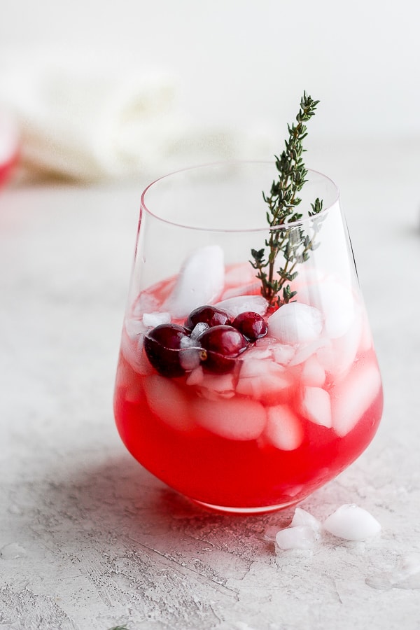 Glass of holiday punch filled halfway with ice, fresh cranberries and sprig of fresh thyme. 