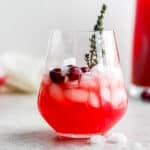 Glass of holiday punch with ice, fresh cranberries and a sprig of fresh thyme.