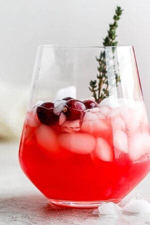 Glass of holiday punch with ice, fresh cranberries and a sprig of fresh thyme.