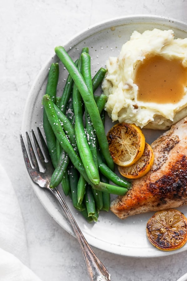 Steamed green beans on a plate with chicken and mashed potatoes.