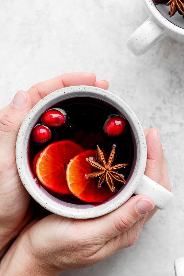 Mulled wine in a white mug and being held by two hands.