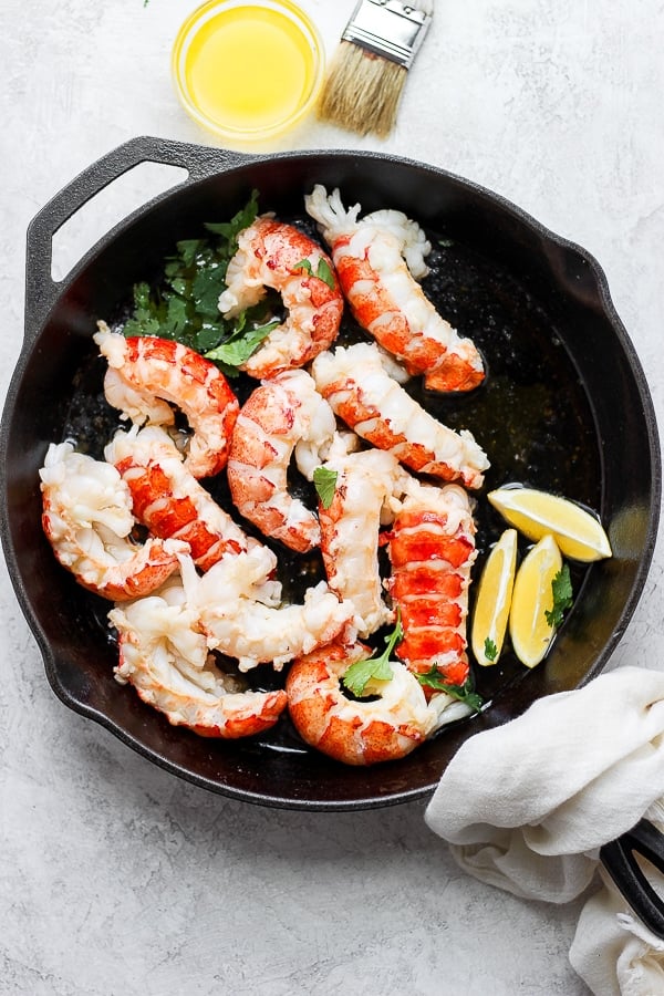 Lobster tails cooking in melted butter in a large skillet.