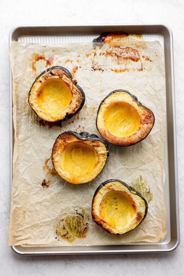 Roasted acorn squash halves on a parchment-lined baking sheet.