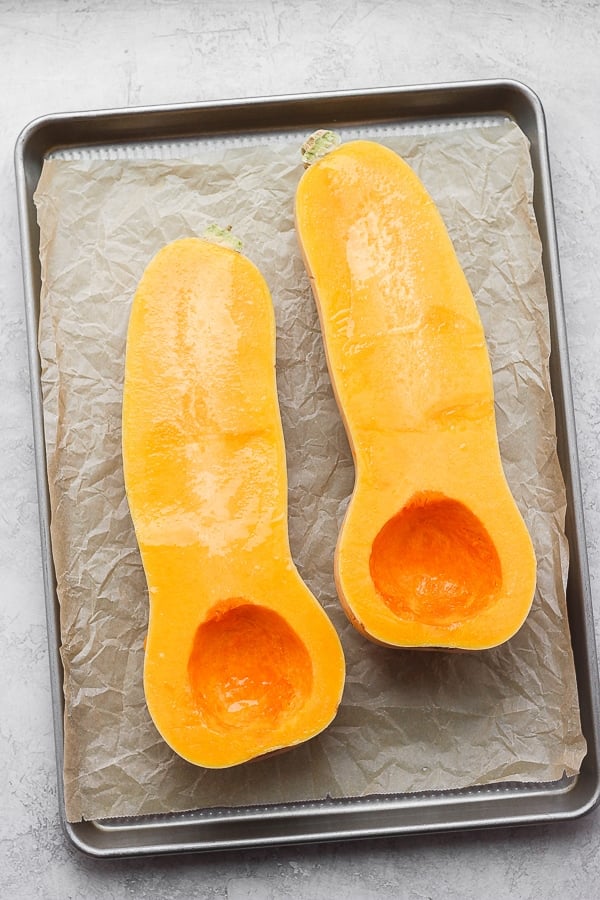 The squash on a parchment-lined baking sheet, the seeds have been scooped out and it was brushed with olive oil.