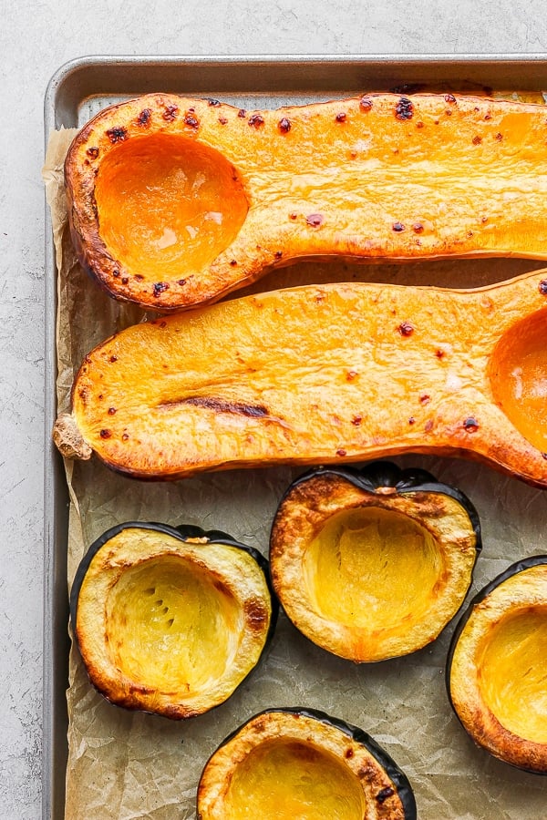 Roasted butternut squash and acorn squash halves on a parchment-lined baking sheet.