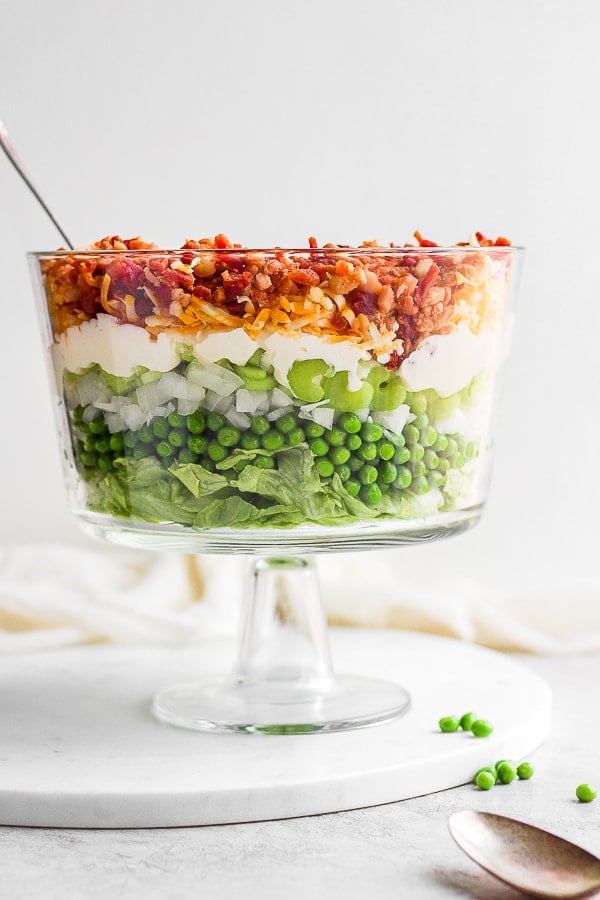 A glass dish with seven layer salad in it and a fork sticking out.