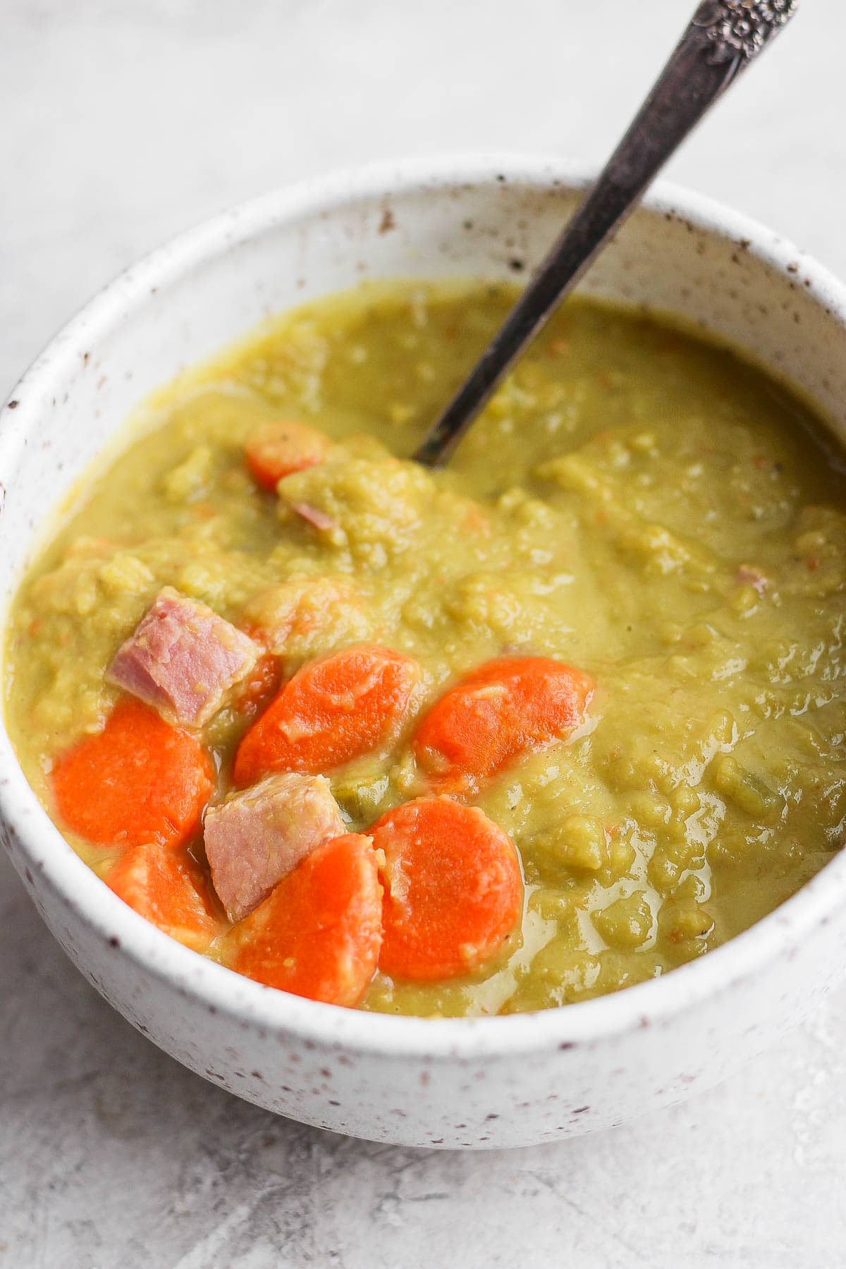 Bowl of split pea and ham soup with a spoon sticking out of it. 