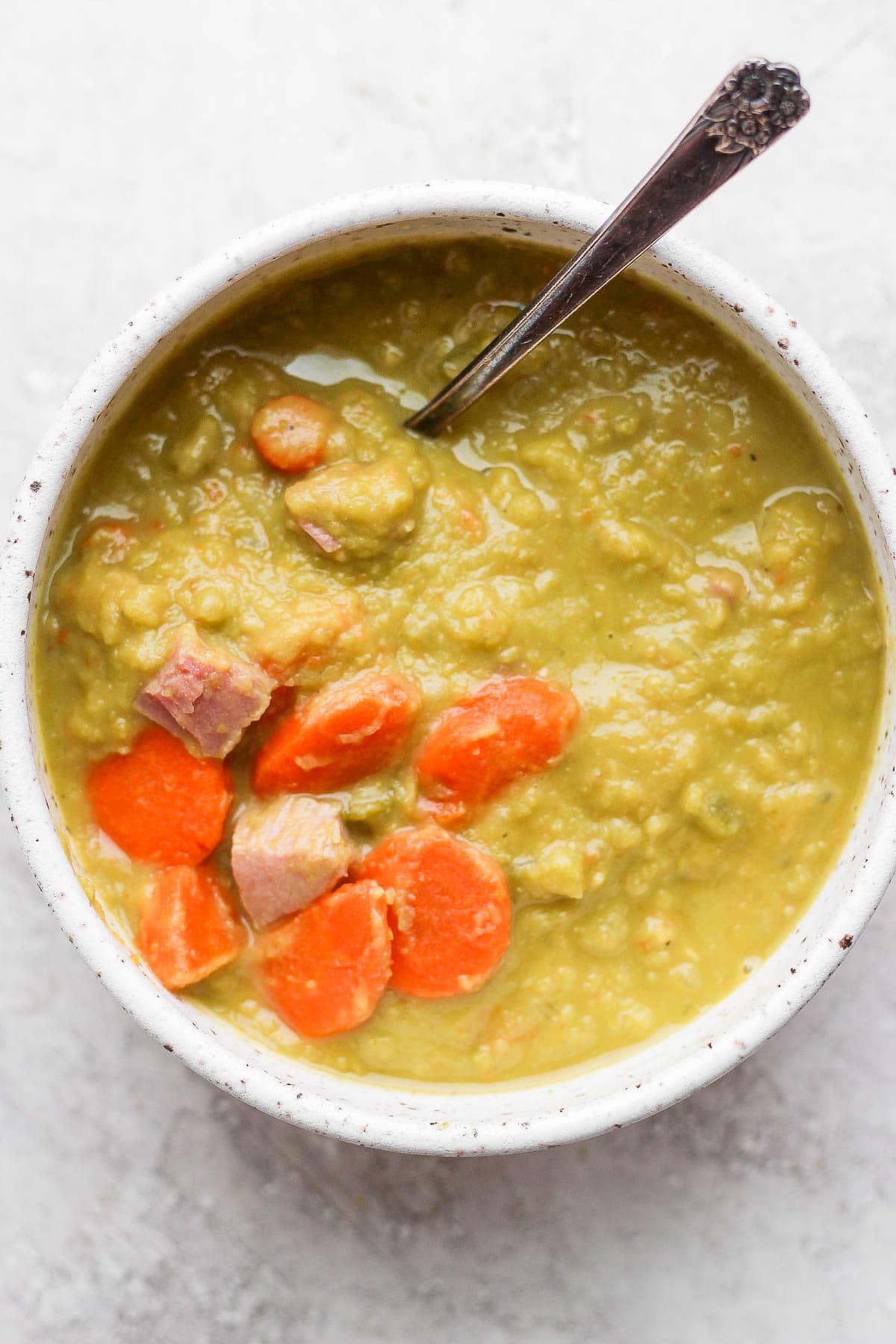 Bowl of split pea and ham soup with a spoon sticking out of it. 