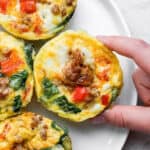 A plate of baked egg cups with someone grabbing one with their fingers.