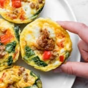 A plate of baked egg cups with someone grabbing one with their fingers.